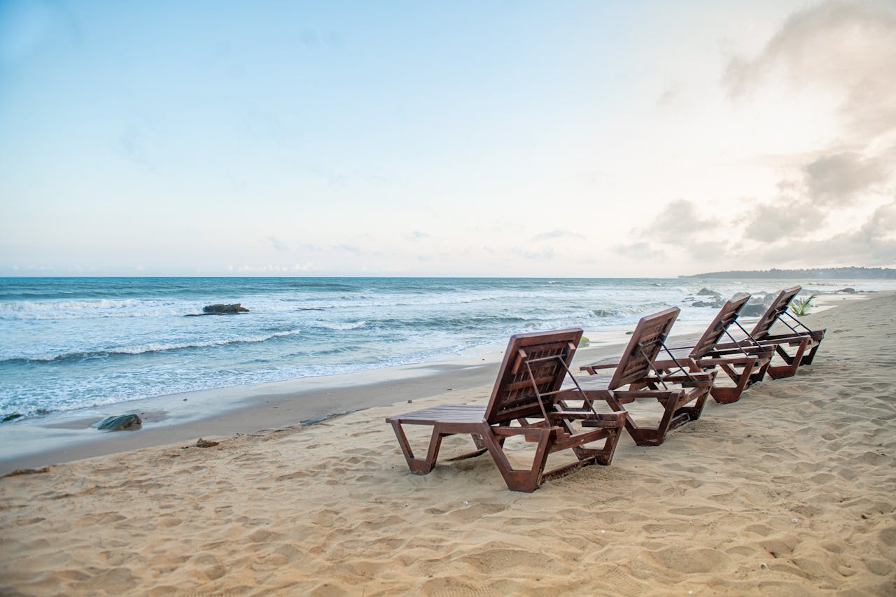 Peaceful beach in Accra, Ghana, featuring wooden loungers on sandy shore against a serene ocean backdrop.